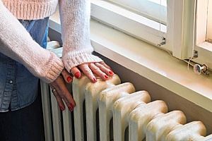 A person is warming their hands by a white radiator.