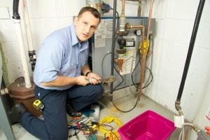 A man in work clothes is crouched, working on a furnace.