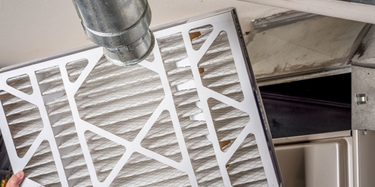 A dirty air filter is being cleaned with a vacuum.