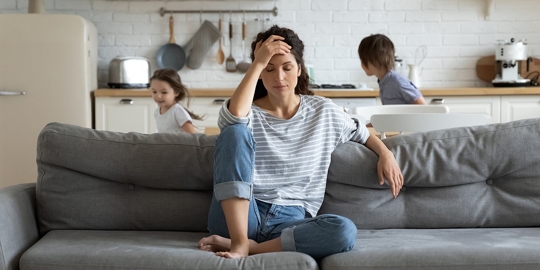 A woman sits on a gray couch, appearing stressed.