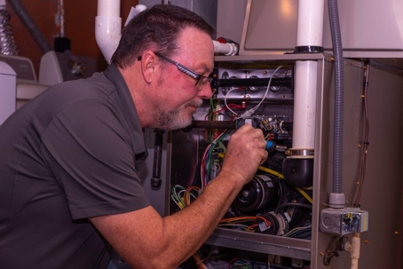 A man in glasses is inspecting a furnace, leaning in close to the interior components.