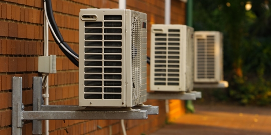 Three white air conditioners mounted on a brick wall.