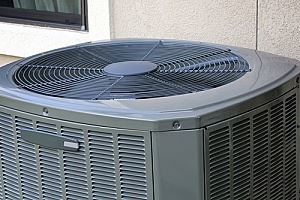 A gray outdoor air conditioner unit with a fan on top.