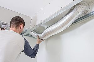 A man is installing metal ductwork in a ceiling.