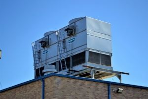 Large, light gray metal cooling units on a rooftop, above a tan-colored building.