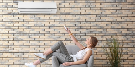 A woman is sitting in a chair, holding an air conditioner remote.