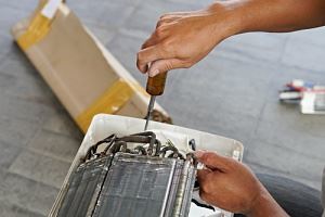 A person is using a screwdriver to work on an air conditioner unit.