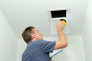 A man is inspecting a ceiling air vent with a yellow flashlight.