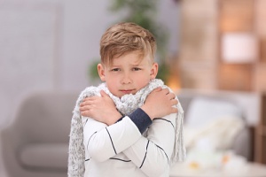 A young boy, bundled in a light gray scarf, looks cold.