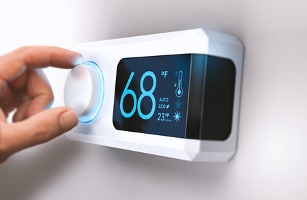 A hand adjusting a digital thermostat set to 68 degrees.