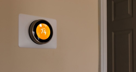 A round, white smart thermostat is mounted on a beige wall.