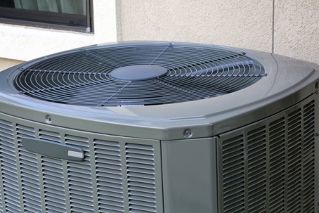 A gray outdoor air conditioner unit with a fan on top.