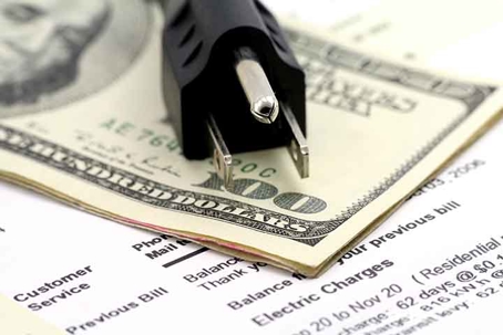 A black electrical plug sits on a dollar bill and utility bill.