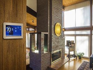 A modern room with a brick fireplace, thermostat, and large windows.