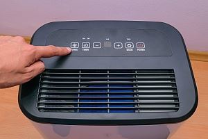 A person's hand is touching the control panel of a small, black and white dehumidifier.