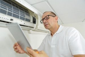 HVAC contractor in Gaithersburg, MD surveying an air conditioning unit while replacing air filters