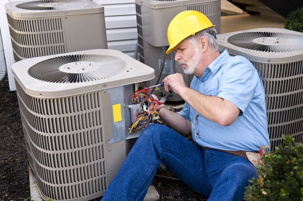 A man in a yellow hard hat is working on an air conditioning unit outdoors.