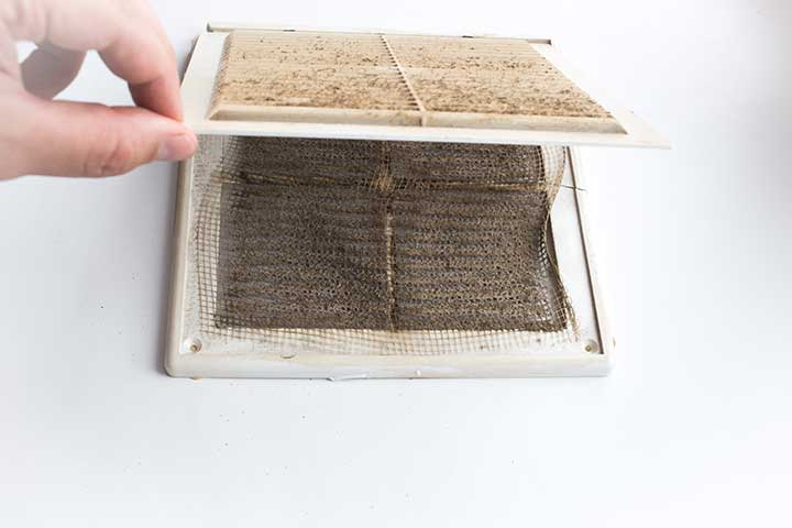 A dirty air vent filter, with a hand lifting the cover.