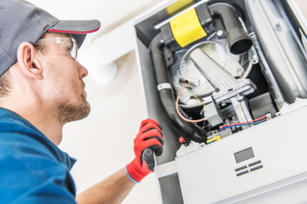 A person in safety glasses and gloves is working on a white wall-mounted heating unit.