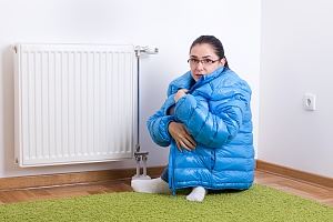 A person in a blue jacket is huddled on the floor near a white radiator