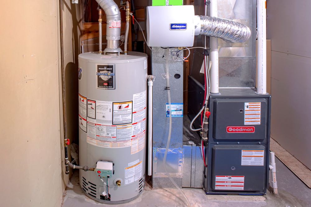 A gray water heater, a blue air cleaner, and a dark gray furnace are in a basement.