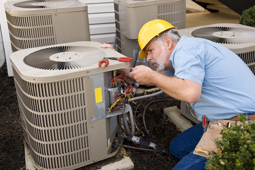 A man in a yellow hard hat is working on air conditioning units outdoors.