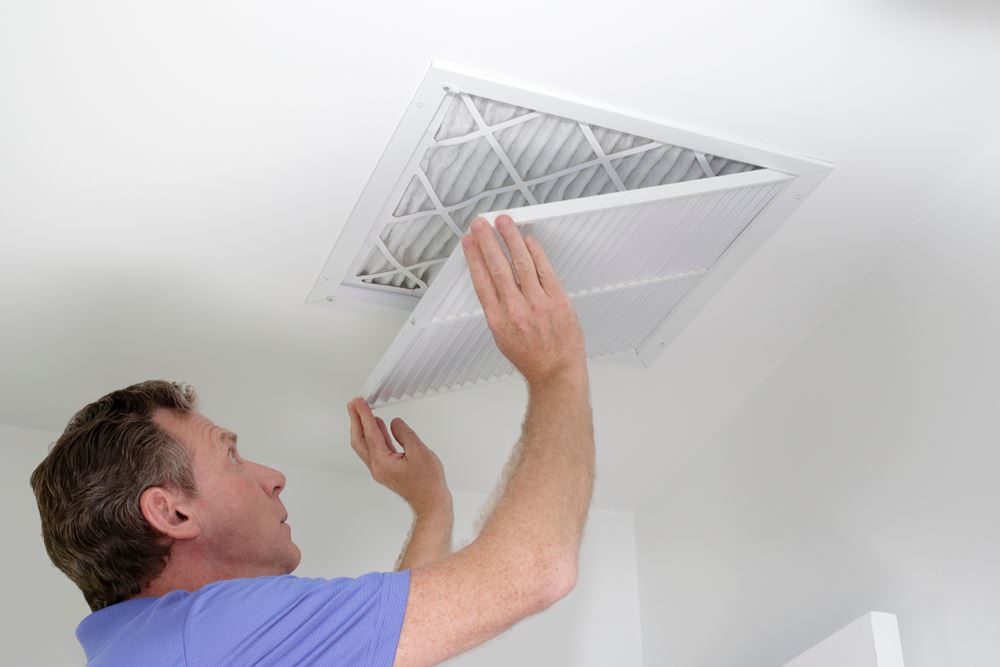 A man is replacing an air filter in a ceiling vent.