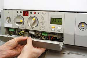A person is working on a gray heating system, opening a panel to access internal components.
