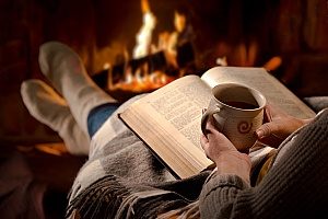 woman reading her book next to the fireplace with hot chocolate in the winter time due to very low humidity in the air as well as relatively cold temperatures