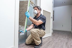 A person in protective gear is cleaning or inspecting an air conditioning filter.
