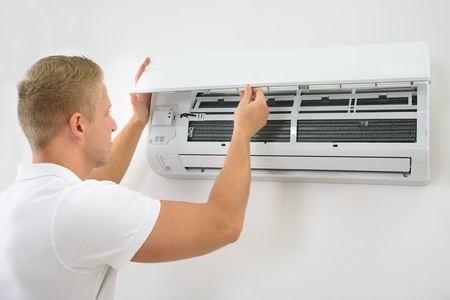 A man is working on an air conditioning unit, likely cleaning or maintaining it.