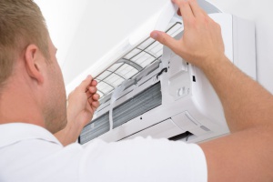 A person is working on an air conditioner unit, removing or cleaning a part.