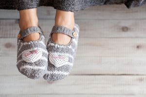 Gray slipper socks with heart designs, on a light-colored wooden floor.
