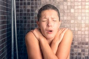 A woman in a shower, appearing cold and shivering.