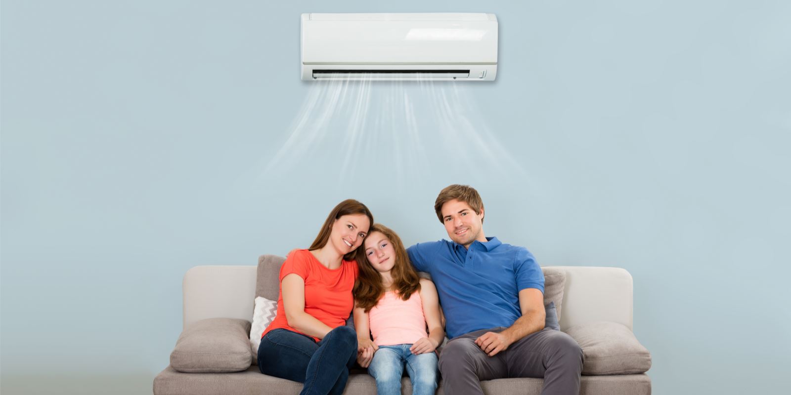 A family sits on a couch; an air conditioner is above them.