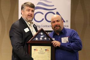 Two men, one holding a framed certificate and American flag display.