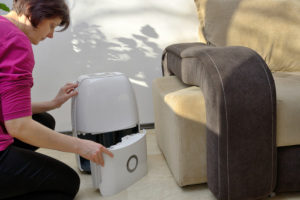 a woman emptying the extracted water out of a portable dehumidifier