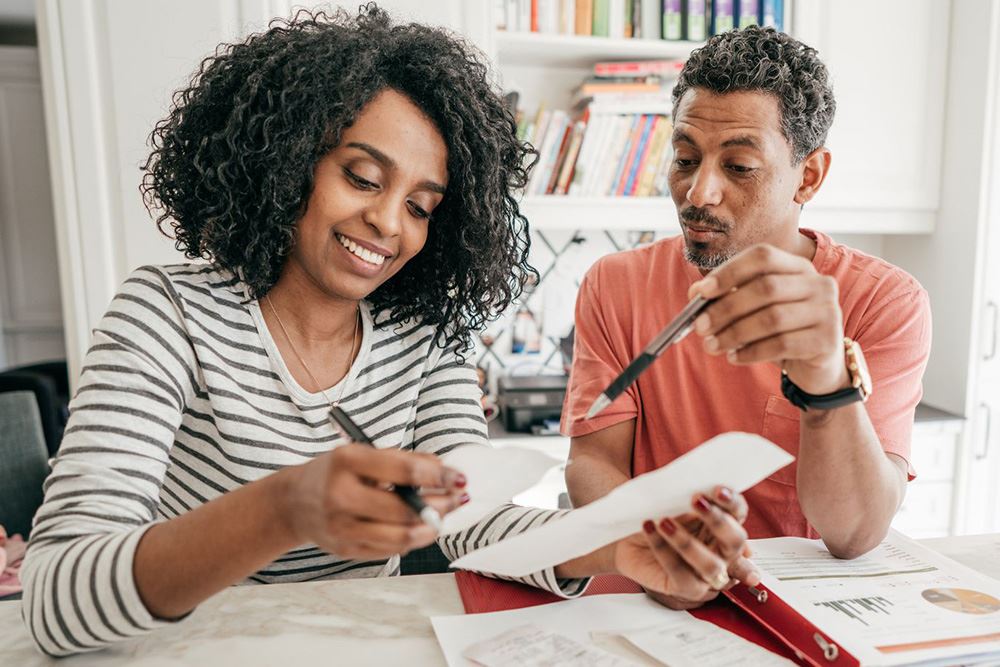 A couple sits at a table, looking at papers.