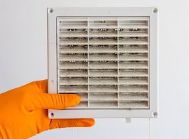 dirty air duct held up by a HVAC contractor wearing an orange gloves