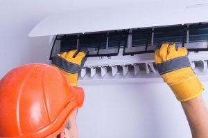 HVAC technician with a hard hat on in Gaithersburg, MD tweaking an HVAC system so that the homeowner will not need AC repair