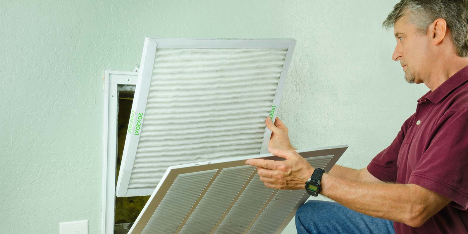 A person is replacing an air filter. The filter is white and pleated.