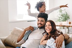 A happy family, a young girl playfully perched on a parent's shoulders, smiling and laughing.