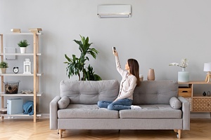 woman on couch using remote to control central air conditioning