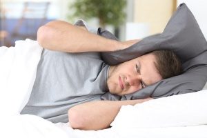 man in bed covering his ears with his pillow due to his HVAC machine emitting loud noises, which is among the most common HVAC problems