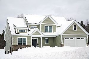 A light olive-green house with a white roof, covered in snow.