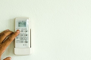 A hand is adjusting a white wall-mounted air conditioner remote.
