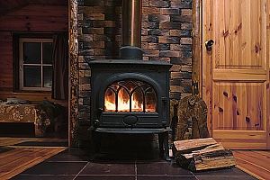 A black wood-burning stove with a fire, dark tile floor, and wooden walls.